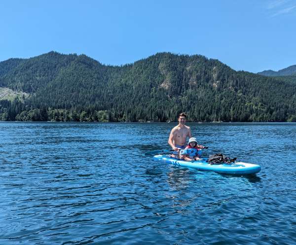 Photograph of Colton sitting on stand-up paddleboard with daughter in Lake Cushman.